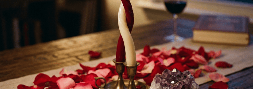 Love letter with candles, rose petals, crystals, and a pen on a wooden table
