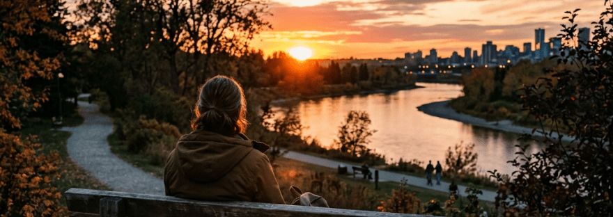 Person on bench overlooking river and city skyline during sunset
