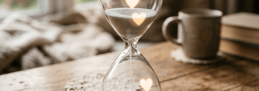 Hourglass with white sand and heart-shaped light reflections on a wooden table