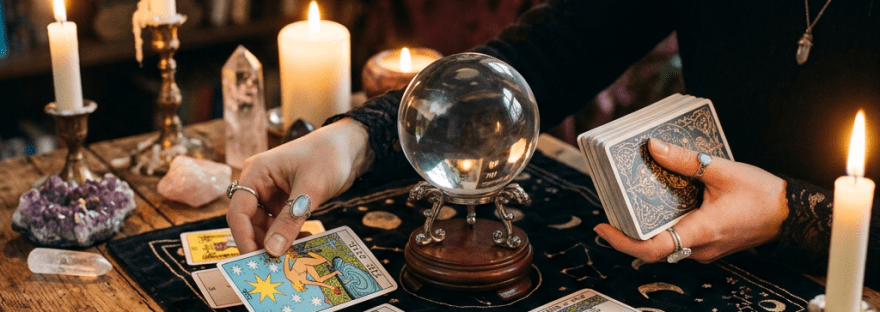 Hands arranging tarot cards on a cloth with a crystal ball and candles nearby