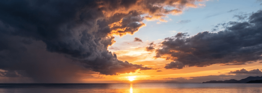 Sunset over ocean with dark storm clouds and calm water reflecting the sky